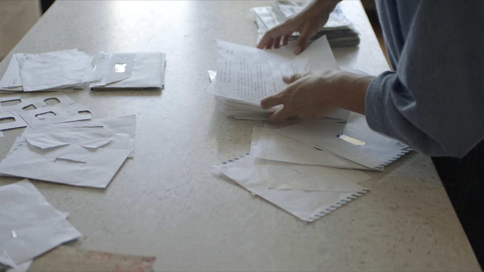 Two hands sorting a spread of window envelopes and folded notices into piles across a kitchen counter in daylight.